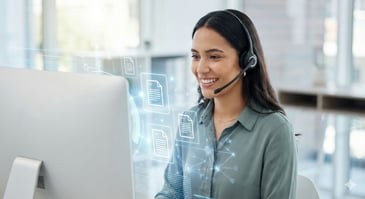  A professional customer service agent wearing a headset and smiling at a computer screen that displays floating holographic knowledge articles and data nodes, illustrating the efficiency of AI Knowledge Management in a modern contact center.